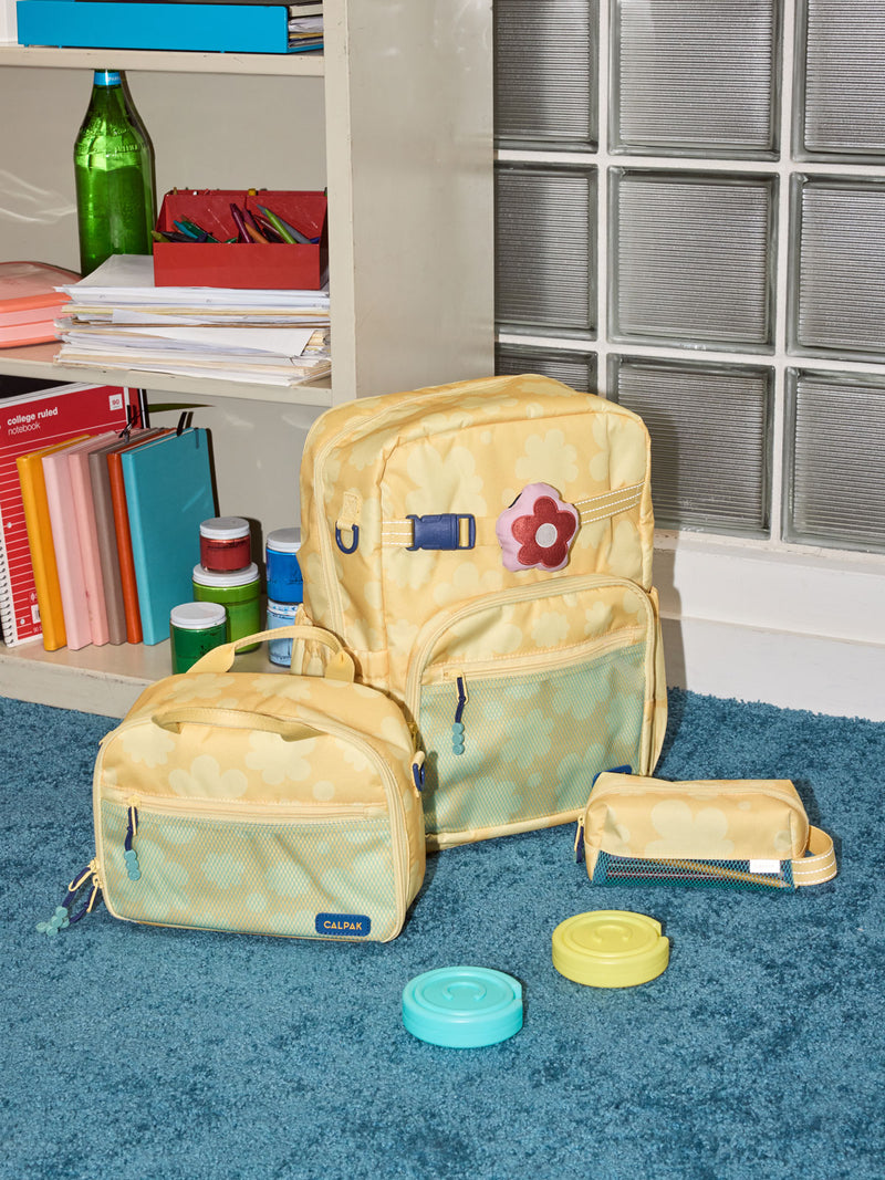 CALPAK Kids Collection Large Kids Backpack Bundle in yellow flower print Yellow Bloom that includes Kids Lunch Bag, Kids Pencil Case, red Car Pluffy Bag Charm, and Set of 2 Ice Packs in a kid's room