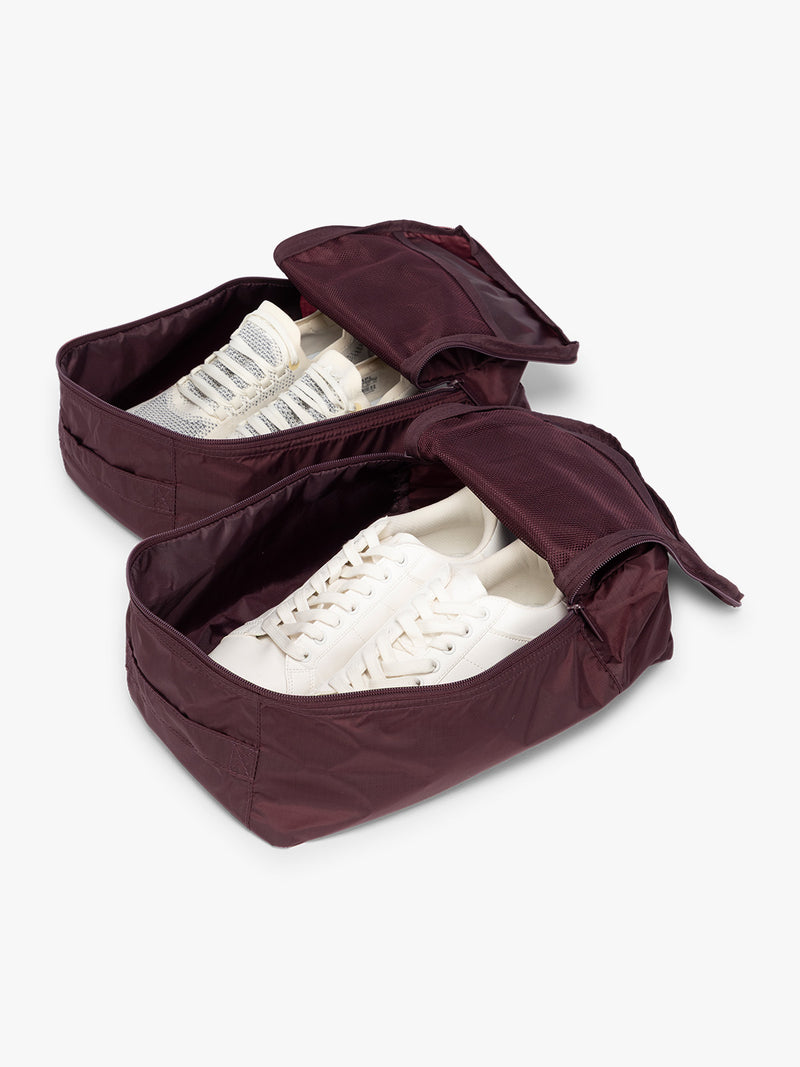 Opened view with shoes inside the burgundy Dark Cherry rectangular CALPAK shoe cube with zippers and top handle shown on a plain background