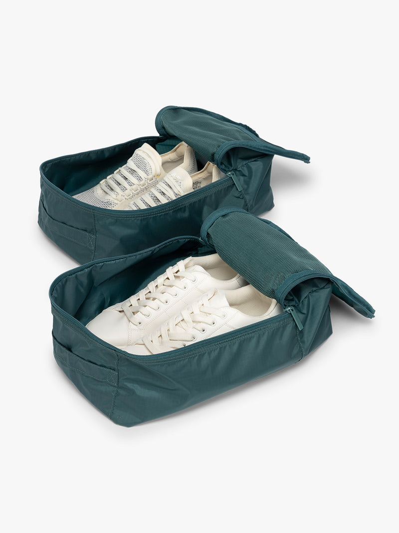 Opened view with shoes inside the dark green teal Kale rectangular CALPAK shoe cube with zippers and top handle shown on a plain background