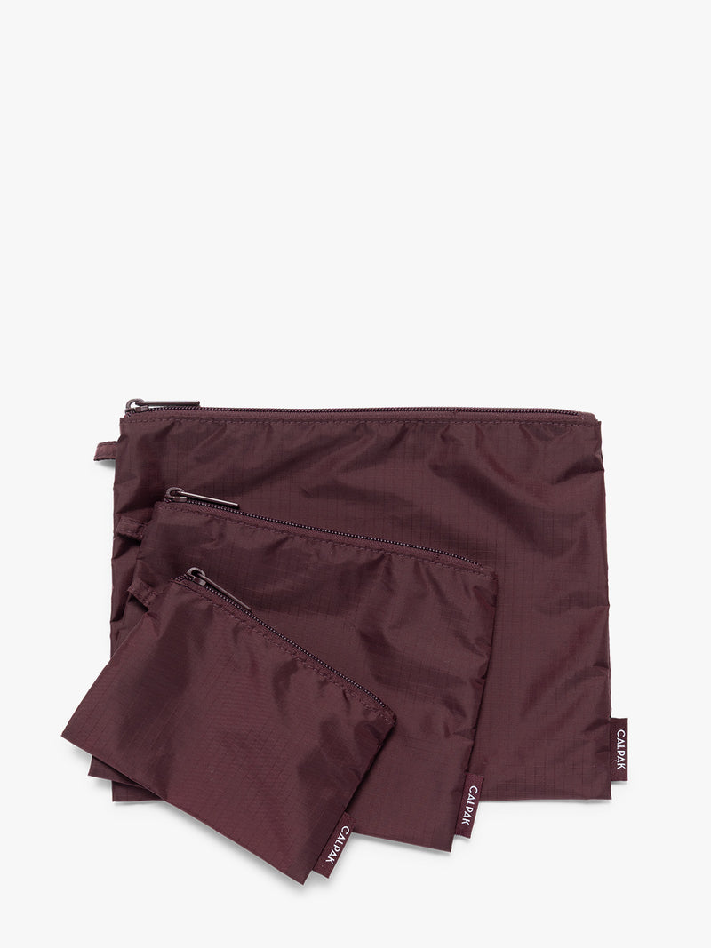 Three burgundy Dark Cherry CALPAK Compakt Zippered pouches of different sizes, arranged in a fan-like layout on a clean white background