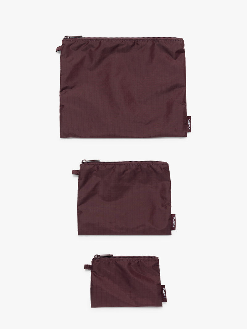 Flat lay of three burgundy Dark Cherry CALPAK Compakt Zippered pouches of different sizes, on a clean white background
