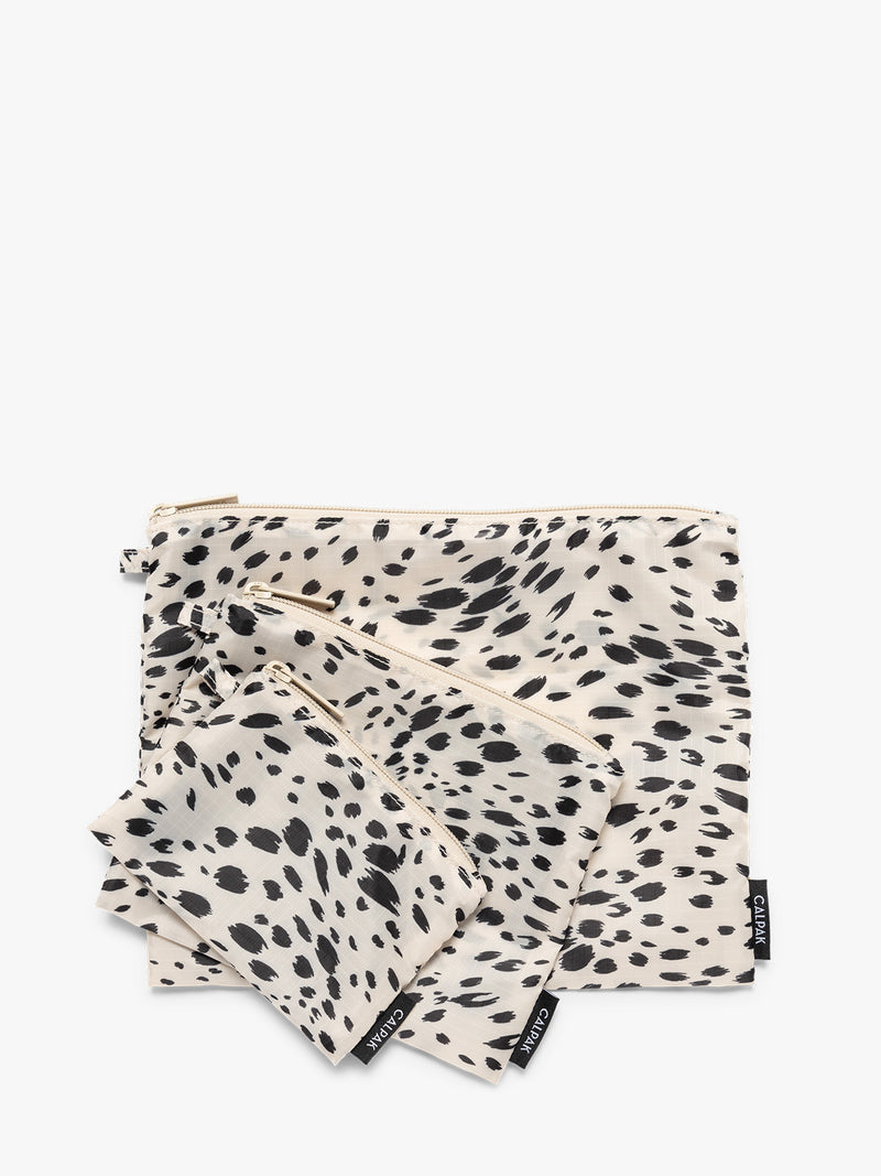 Three white and black animal print Snow Leopard CALPAK Compakt Zippered pouches of different sizes, arranged in a fan-like layout on a clean white background