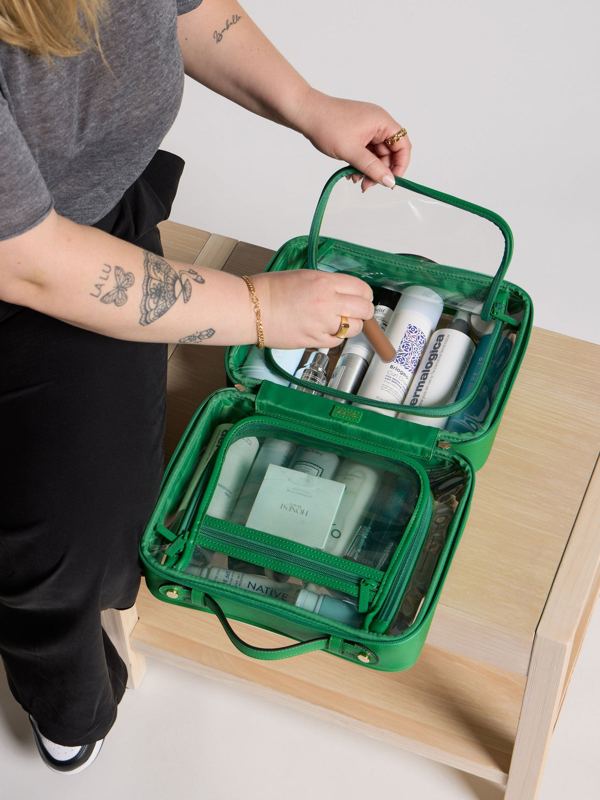 Model placing makeup inside CALPAK Large Clear Cosmetic Case for women; CCC2001-GREEN-APPLE