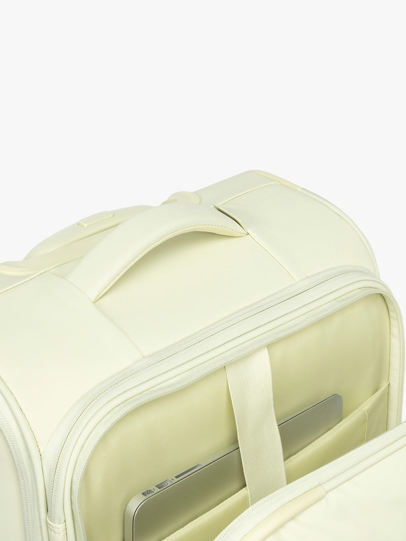 Top grab handle and front laptop sleeve of the CALPAK Luka Soft-Sided Carry On Luggage in light green Celadon on a white background with handle and spinner wheels