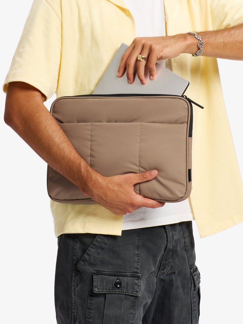 Model placing 14 inch laptop into main pocket of CALPAK Luka 14" Padded Laptop Sleeve in chocolate brown