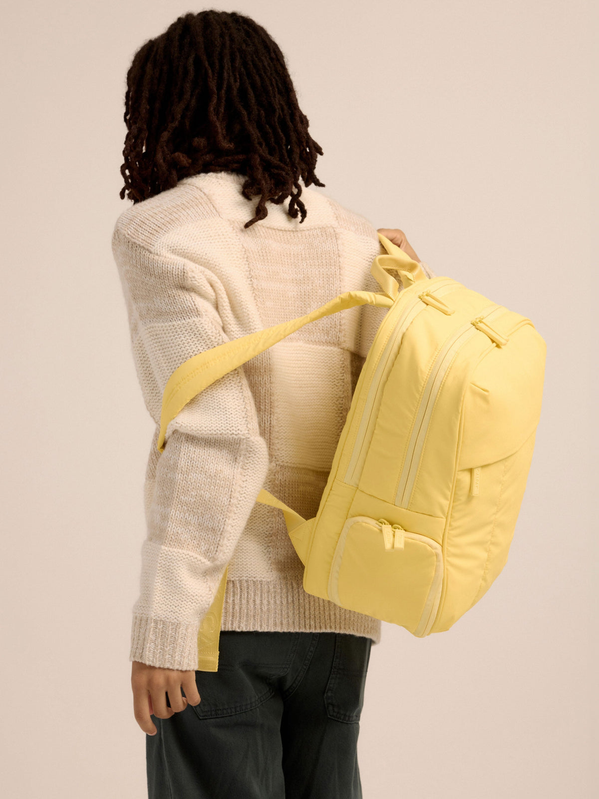 Model placing adjustable shoulder straps of yellow CALPAK Luka 15 inch Laptop Backpack over shoulders; BPL2001-BUTTER
