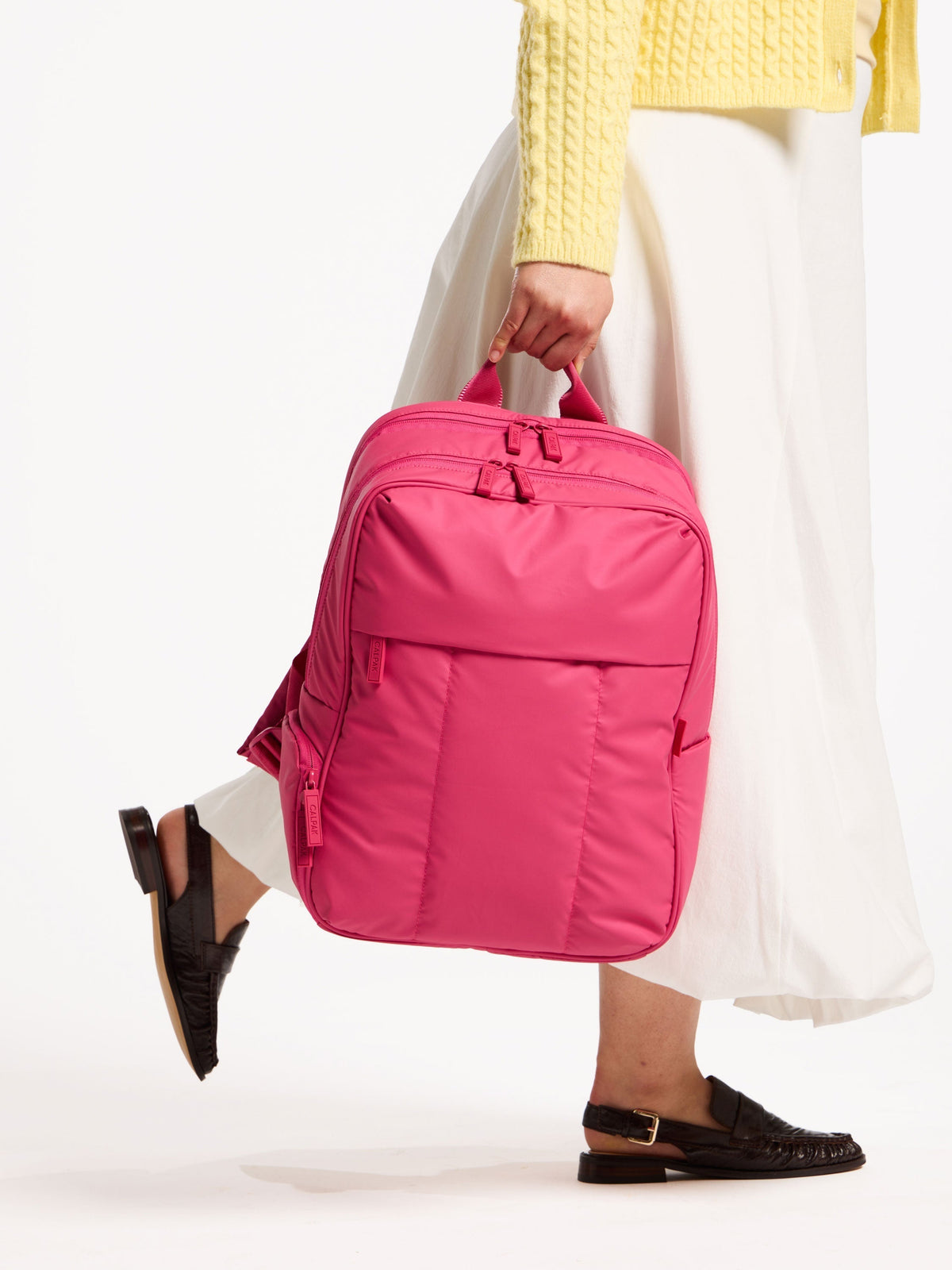 Model holding CALPAK luka 15 inch laptop backpack by top handle in dragonfruit; BPL2001-DRAGONFRUIT