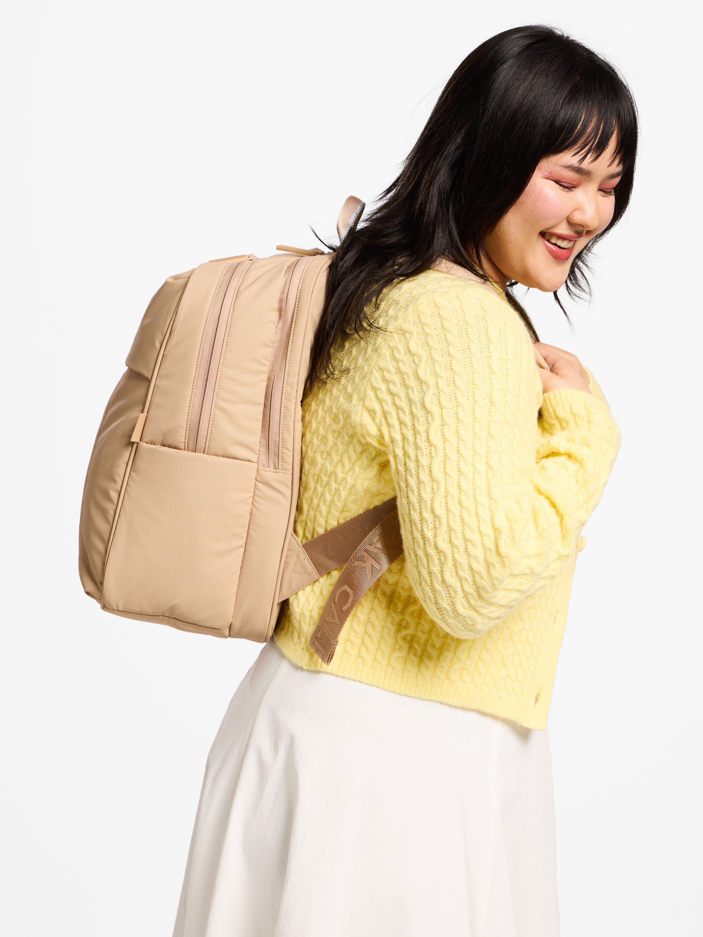 Model wearing latte puffy CALPAK laptop backpack for 15 inch laptop