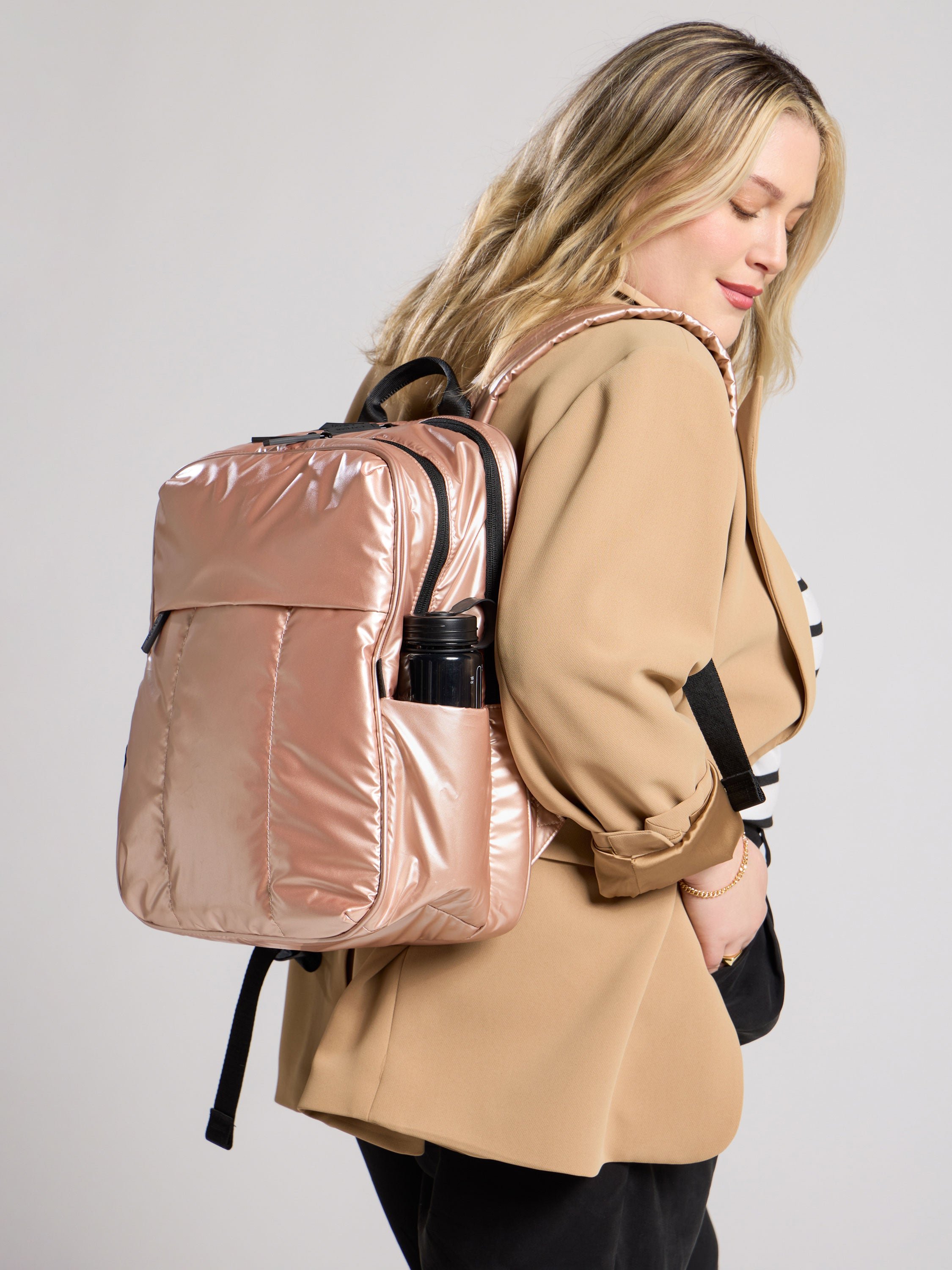 Model wearing Luka 15 inch Laptop Backpack on back with water bottle in exterior pocket in rose gold