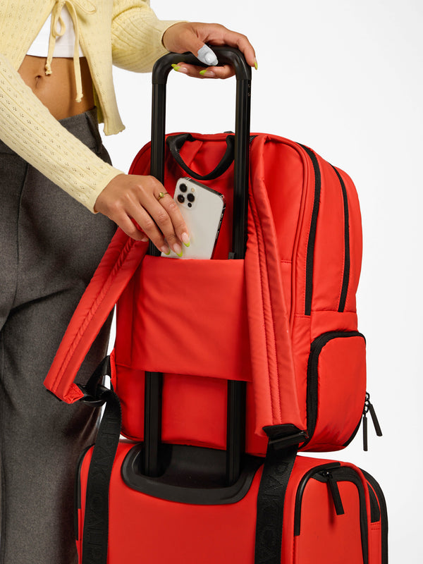 Model placing cellphone inside secret pocket of CALPAK Luka 15 inch Laptop Backpack luggage trolley sleeve in red rouge