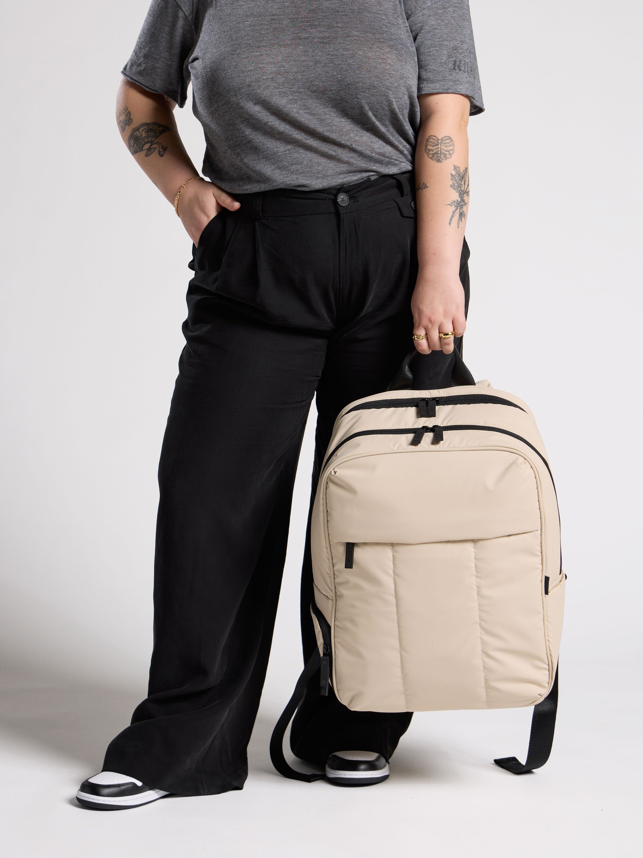 Model holding sofy, puffy CALPAK Luka 17 inch Laptop Backpack in oatmeal with water resistant exterior