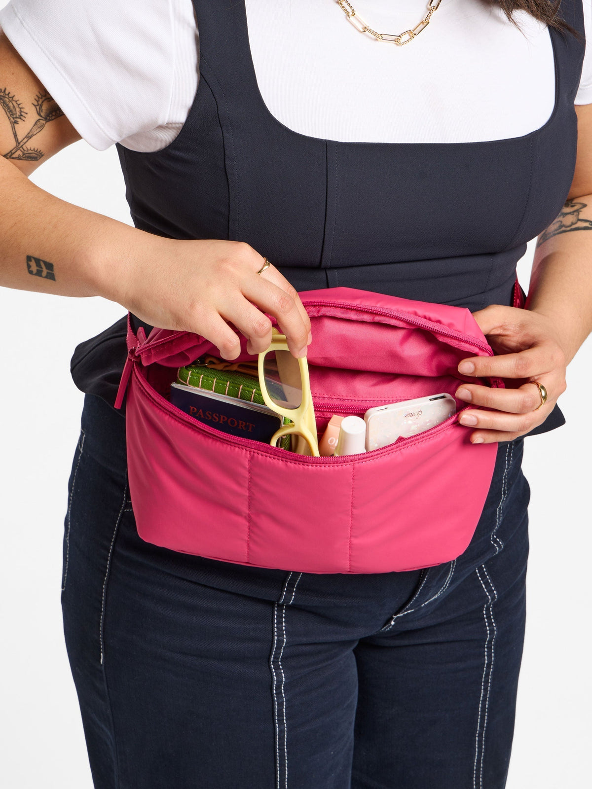 Model placing belongings within main pocket of CALPAK Luka Belt Bag in dragonfruit; BB1901-DRAGONFRUIT