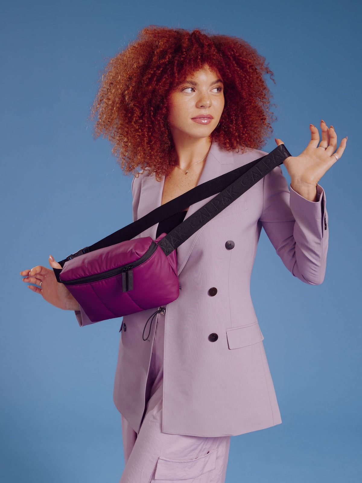 Model holding CALPAK Luka Belt Bag in plum by adjustable strap; BB1901-PLUM