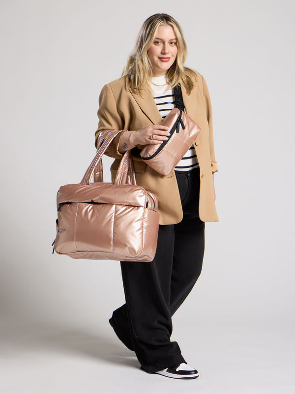 Model wearings metallic rose gold belt bag as crossbody bag and luka duffel bag over shoulder