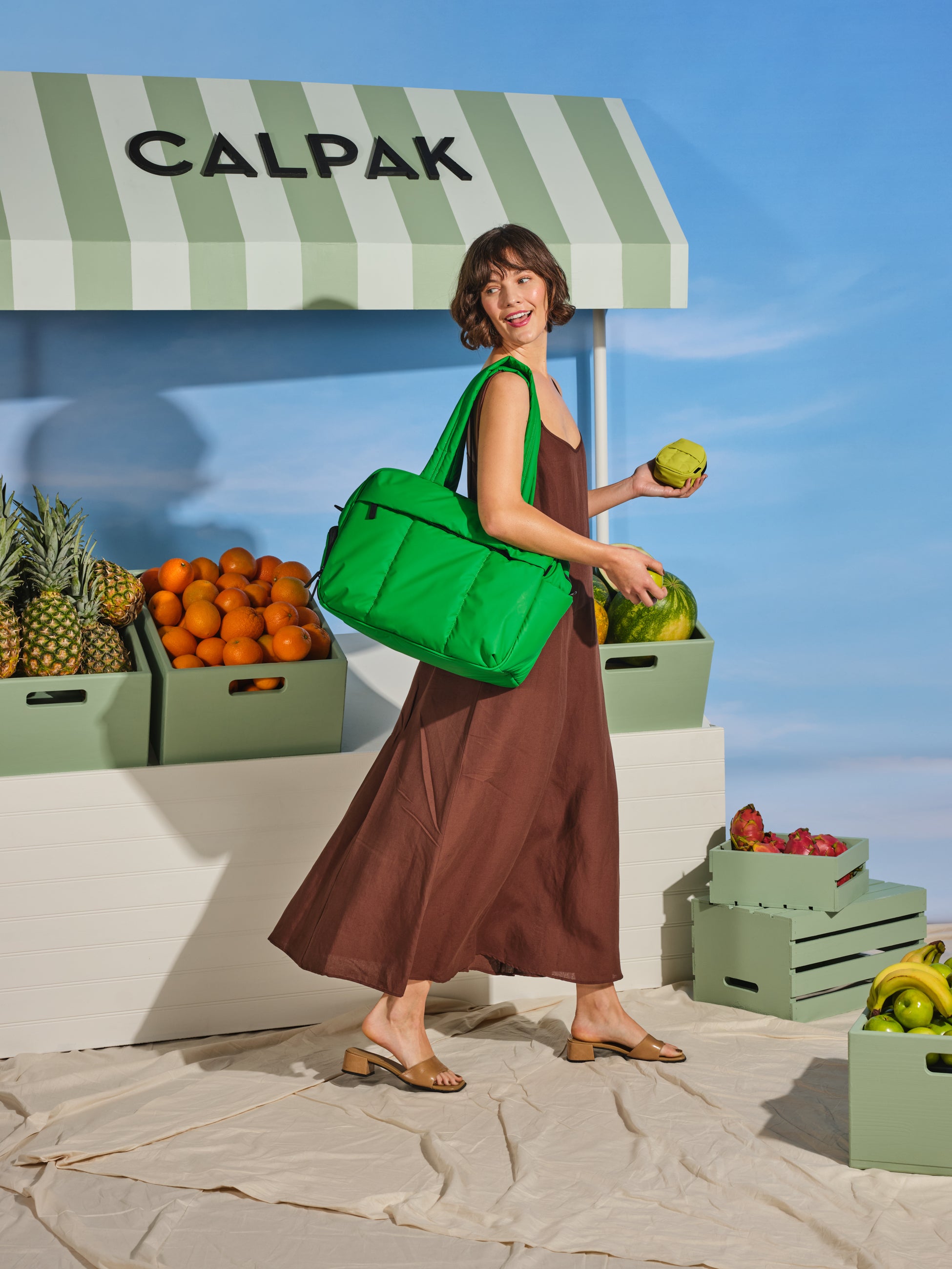 Model carrying CALPAK Luka Duffel Bag with dual straps and front zippered pocket  in green apple