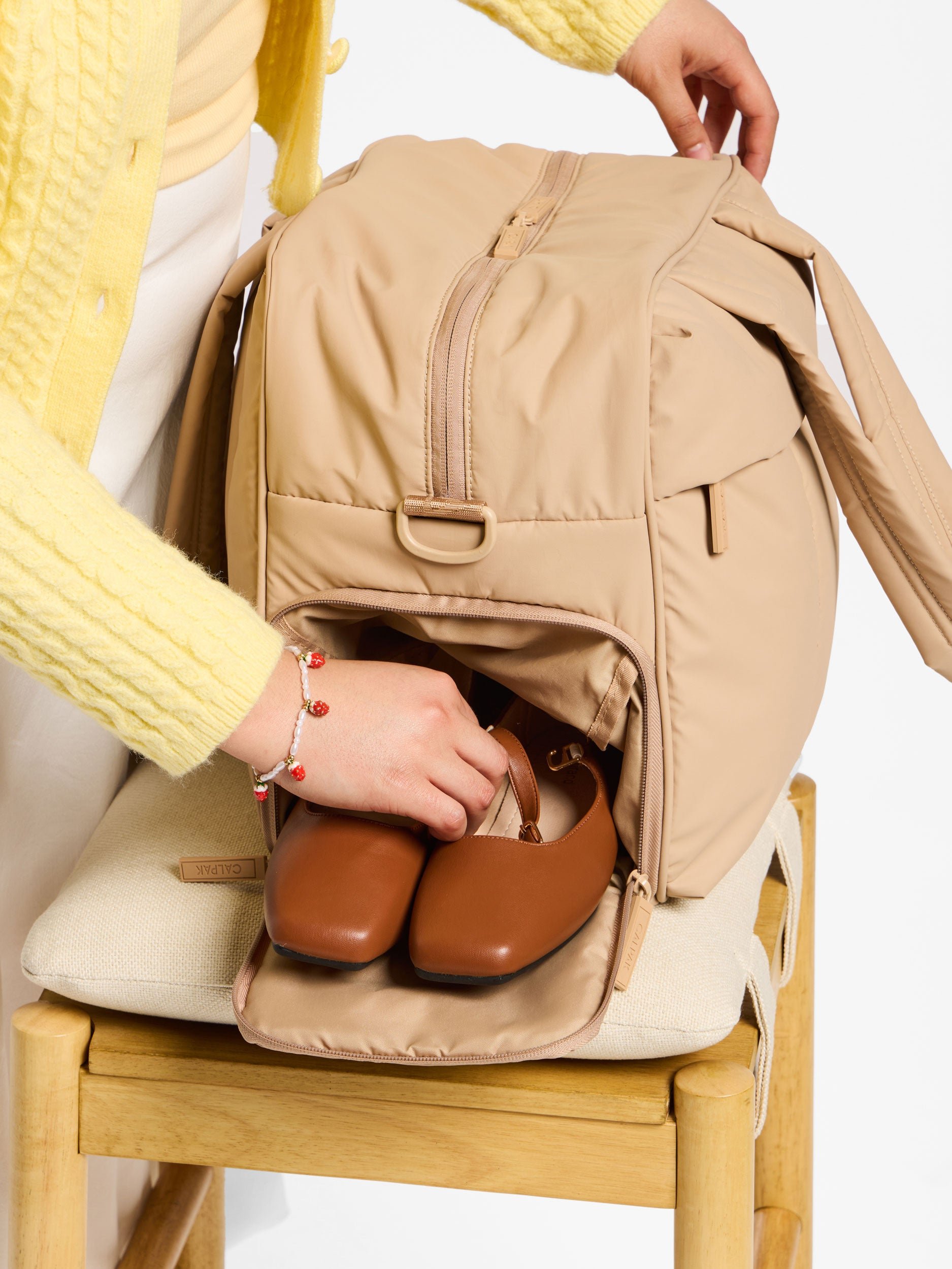 Model placing shoes within shoe compartment of CALPAK luka duffel in light brown