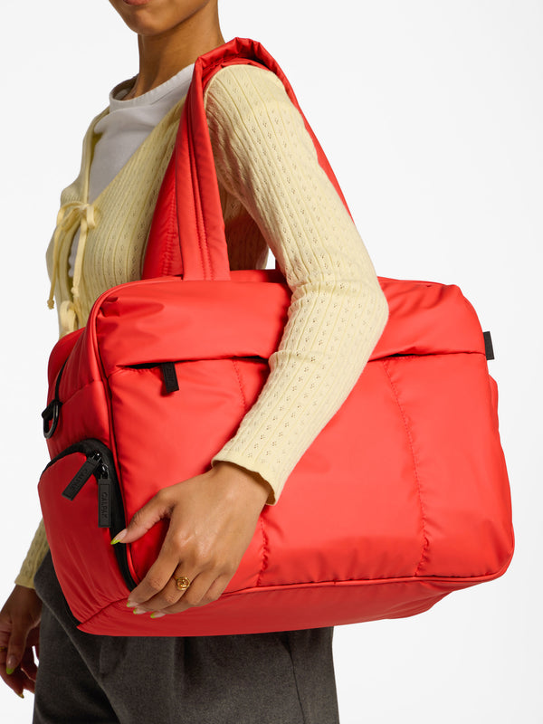 Model holding CALPAK Luka Duffel Bag over shoulder by handle in rouge