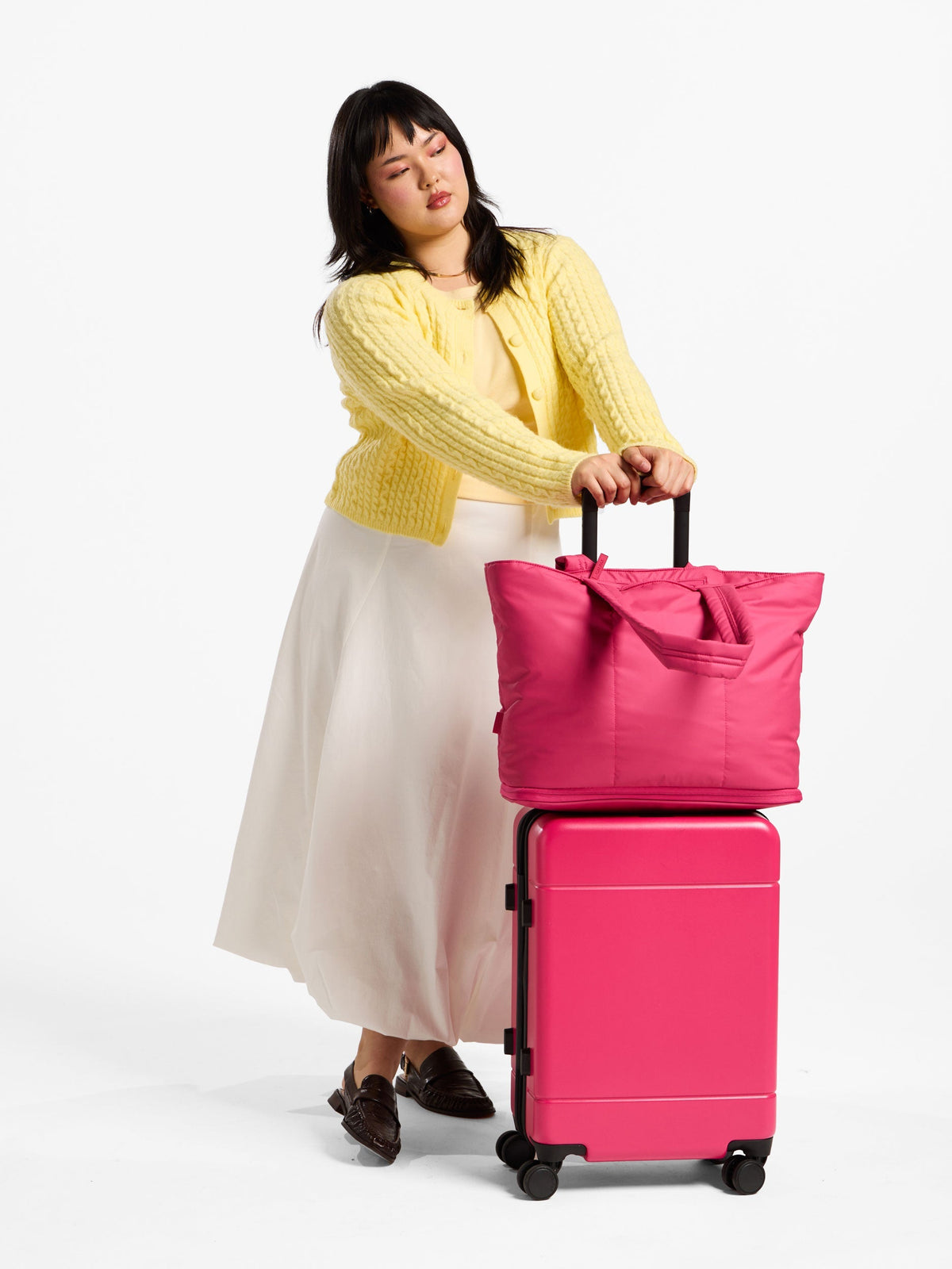 Model stands besides dragonfruit CALPAK Hue Carry On Luggage with Luka Expandable Laptop Tote Bag on top; ALT2201-DRAGONFRUIT