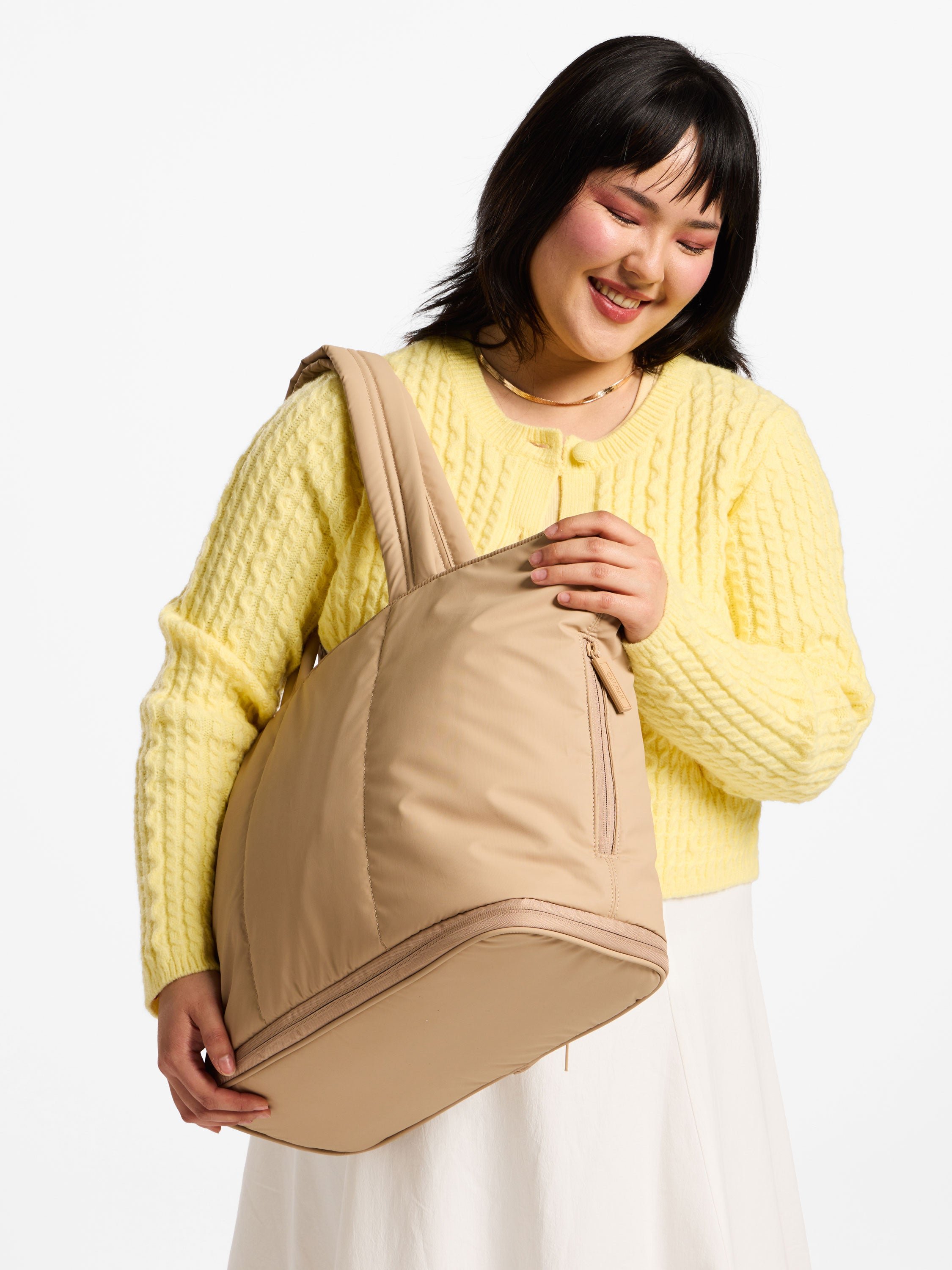 Model carries CALPAK expandable laptop tote bag over shoulder in latte