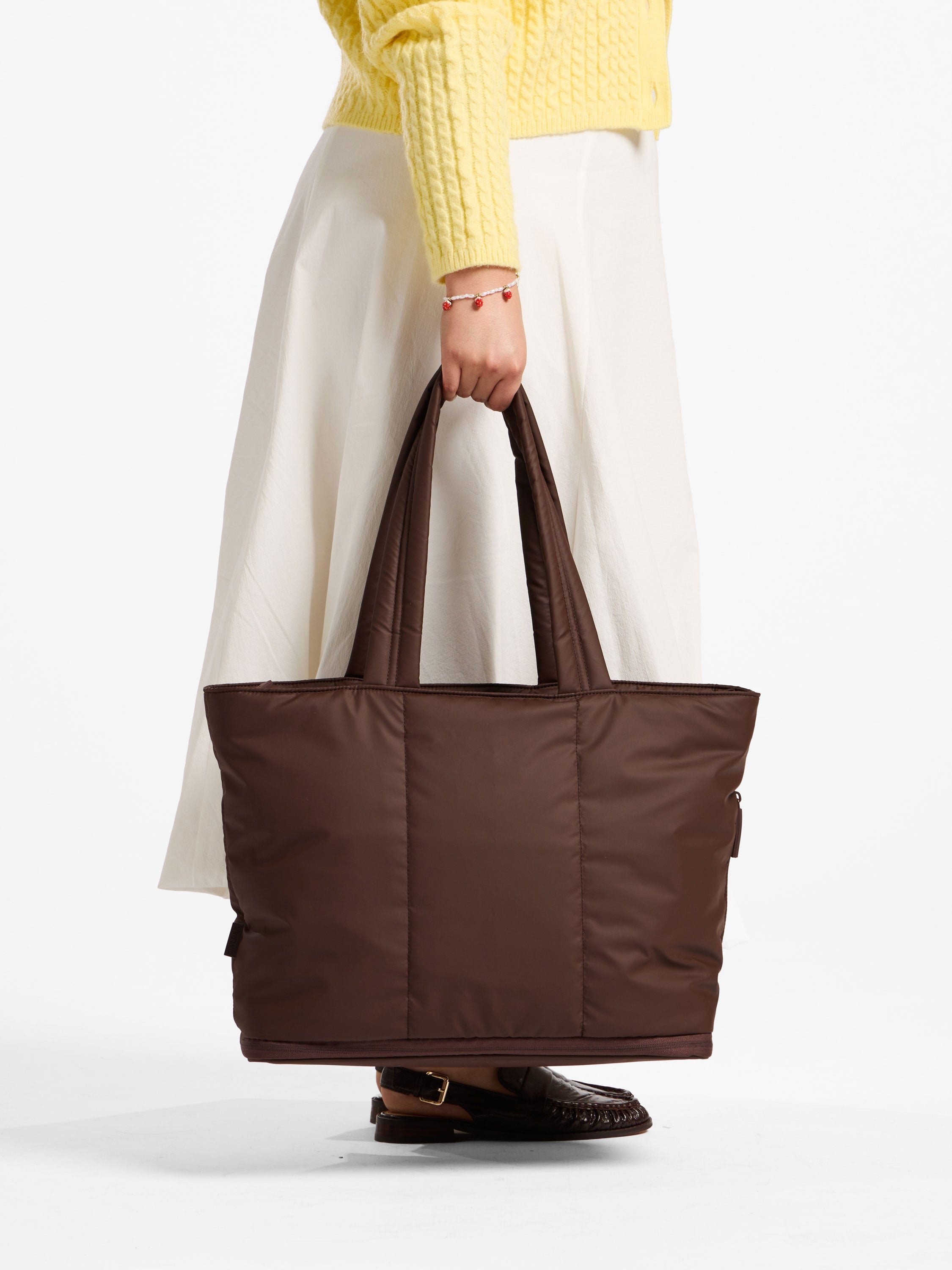 Model holds CALPAK Luka Expandable Laptop Tote Bag by handle in walnut