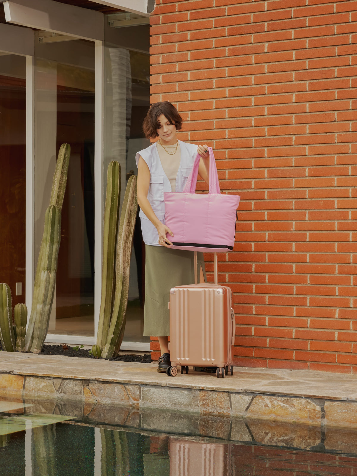 Model placing CALPAK Luka expandable laptop tote bag on carry on with trolley sleeve in bubblegum; ALT2201-BUBBLEGUM
