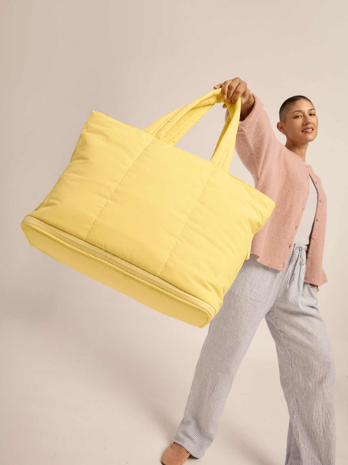 Model holding CALPAK Luka Expandable Laptop Tote by carrying handle in butter yellow; ALT2201-BUTTER
