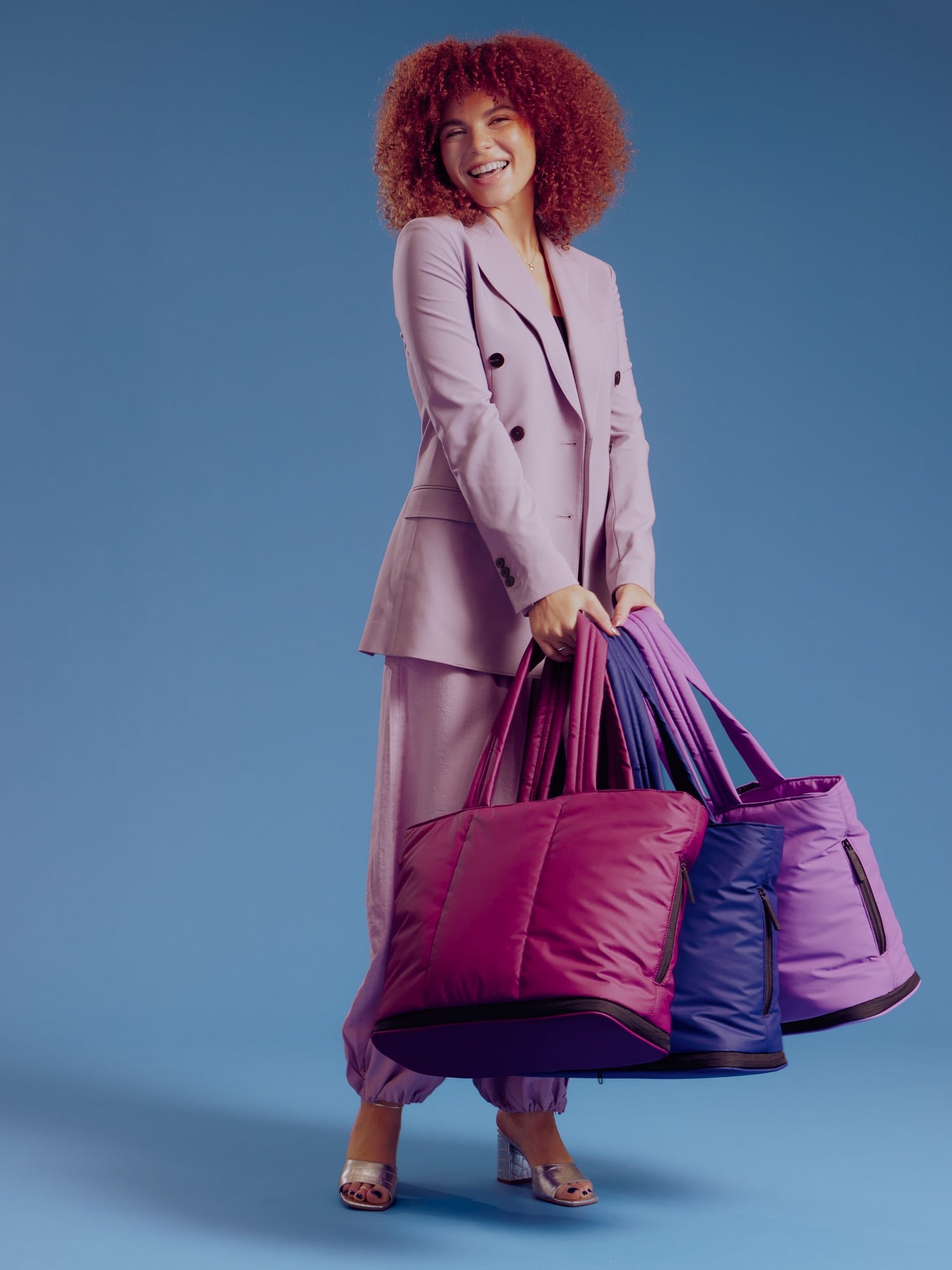 Model holding CALPAK Luka Expandable Laptop Totes in plum, navy, and lilac