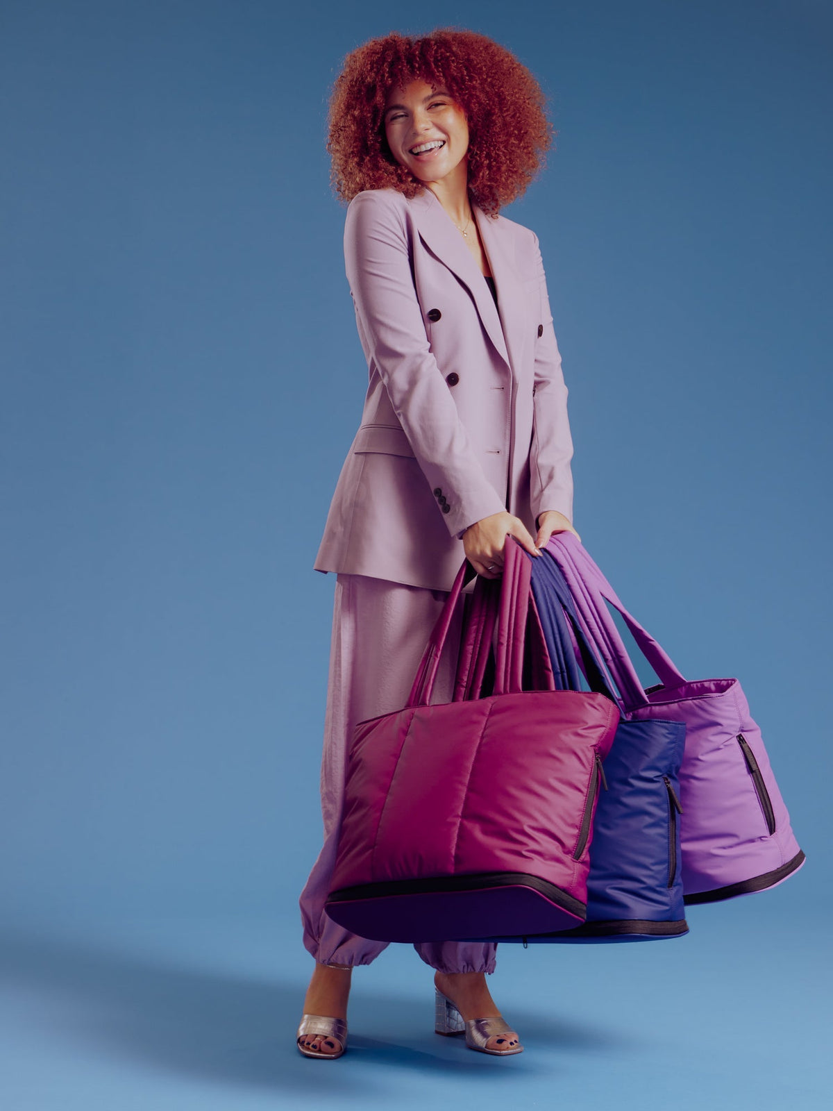 Model holding CALPAK Luka Expandable Laptop Totes in plum, navy, and lilac; ALT2201-PLUM
