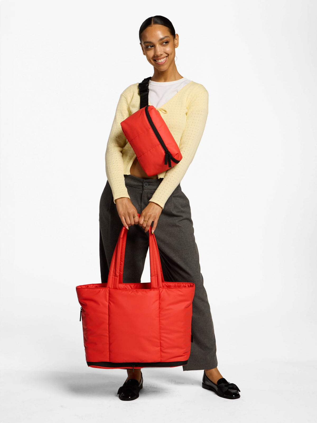 Model wearing CALPAK Luka Belt Bag in rouge as crossbody bag while holding CALPAK Luka Expandable Laptop Tote by handle in red; ALT2201-ROUGE