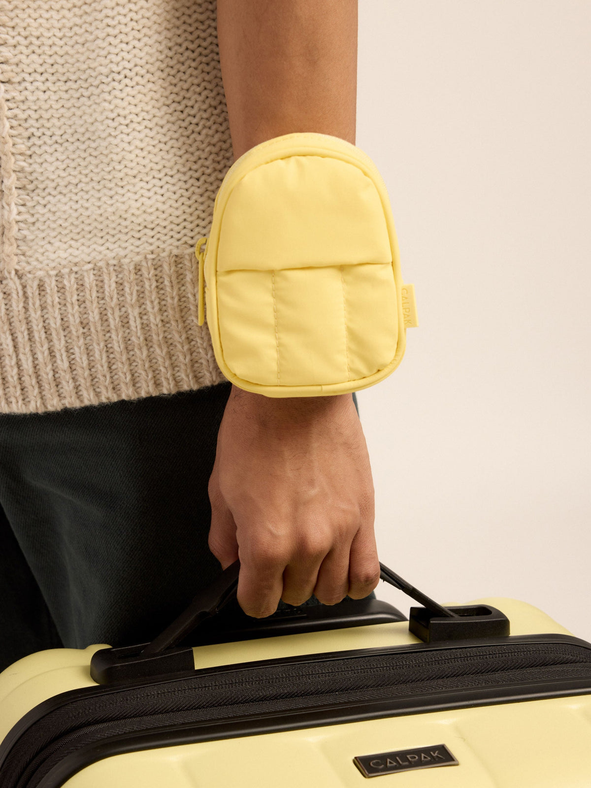 Model wearing CALPAK Luka Key Pouch on wrist in butter yellow; AMB2201-BUTTER