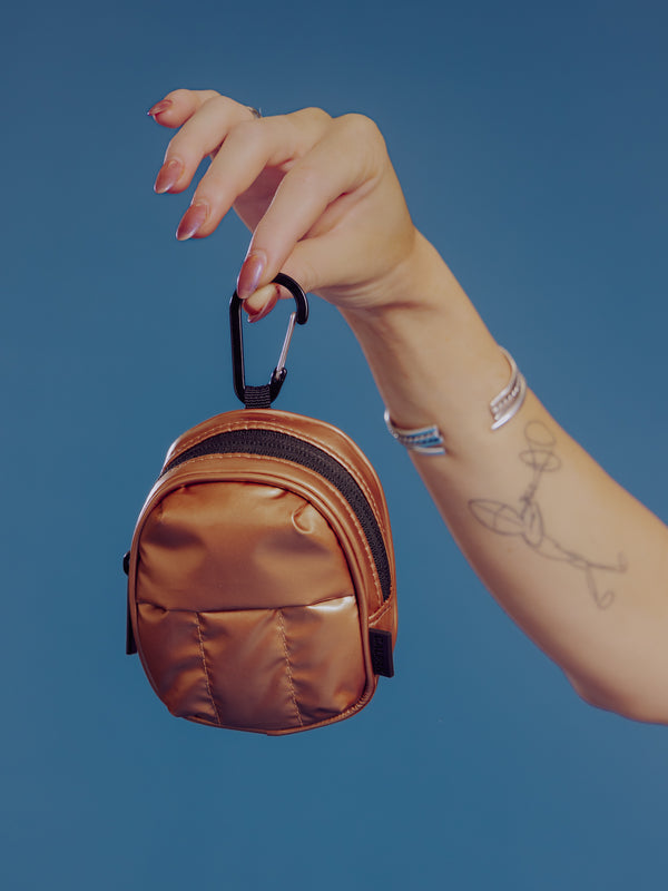 Model holding up CALPAK Luka Key Pouch in copper by the carabiner clip