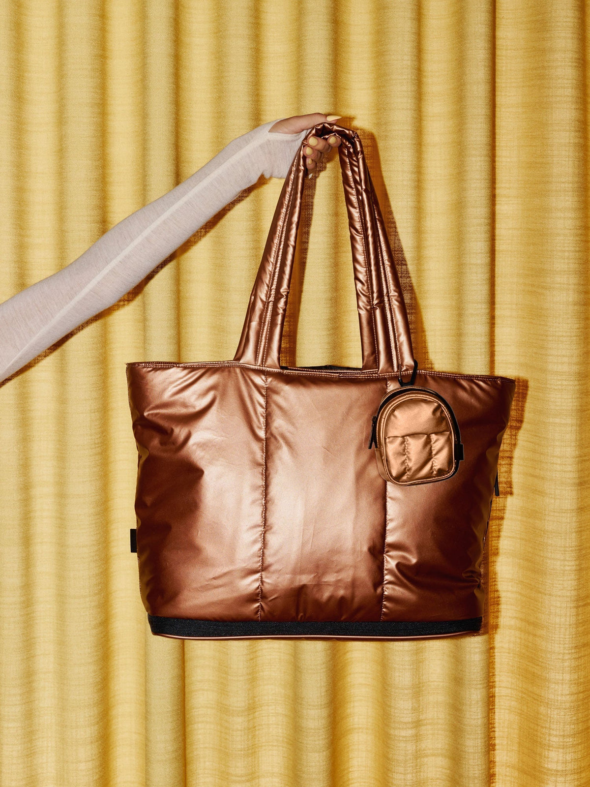 Model holding up CALPAK Luka Expandable Laptop Tote with Luka Key Pouch clipped to strap in copper; AMB2201-COPPER