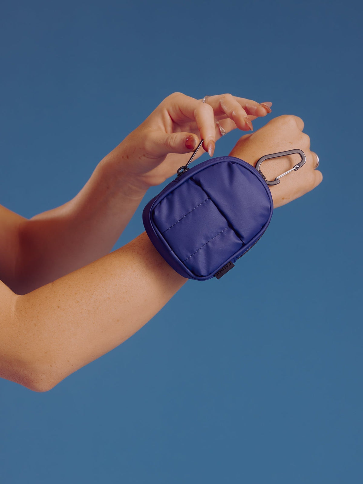Model displaying CALPAK Luka Key Pouch and displaying main pocket zipper in navy; AMB2201-NAVY