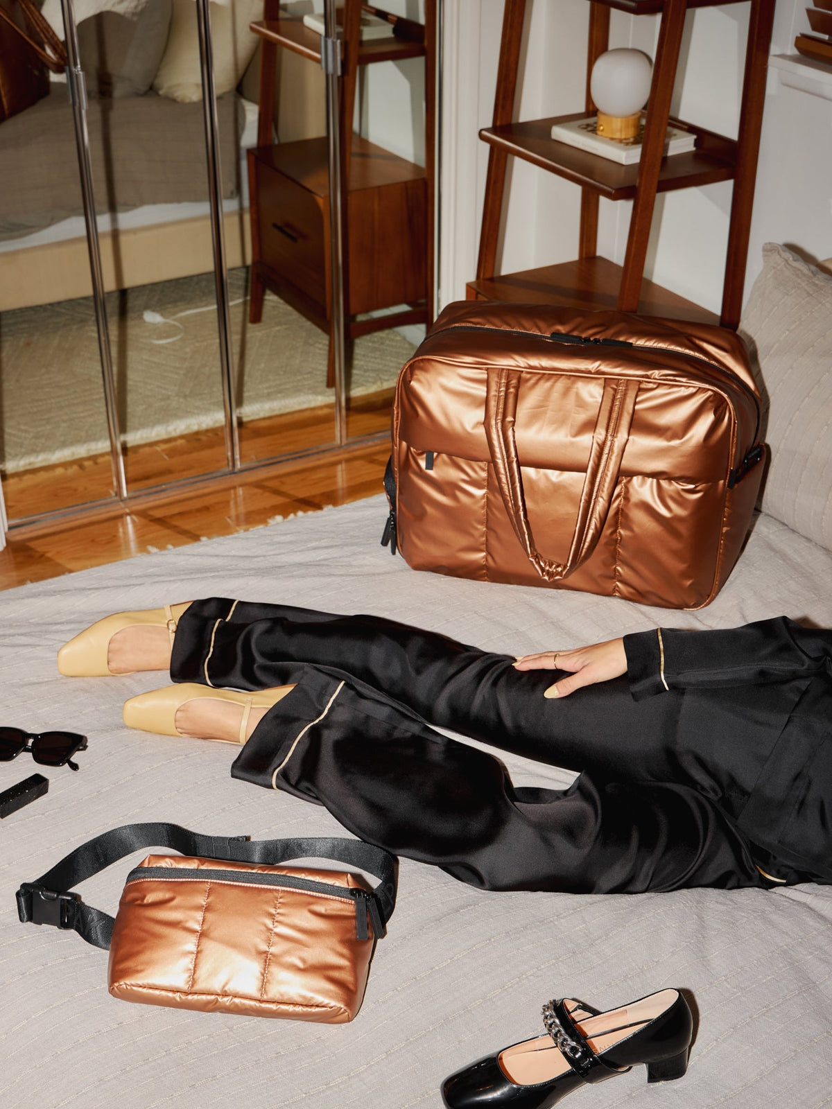 Model laying besides CALPAK Luka Large Duffel and CALPAK Luka Belt Bag in copper; DLL2201-COPPER