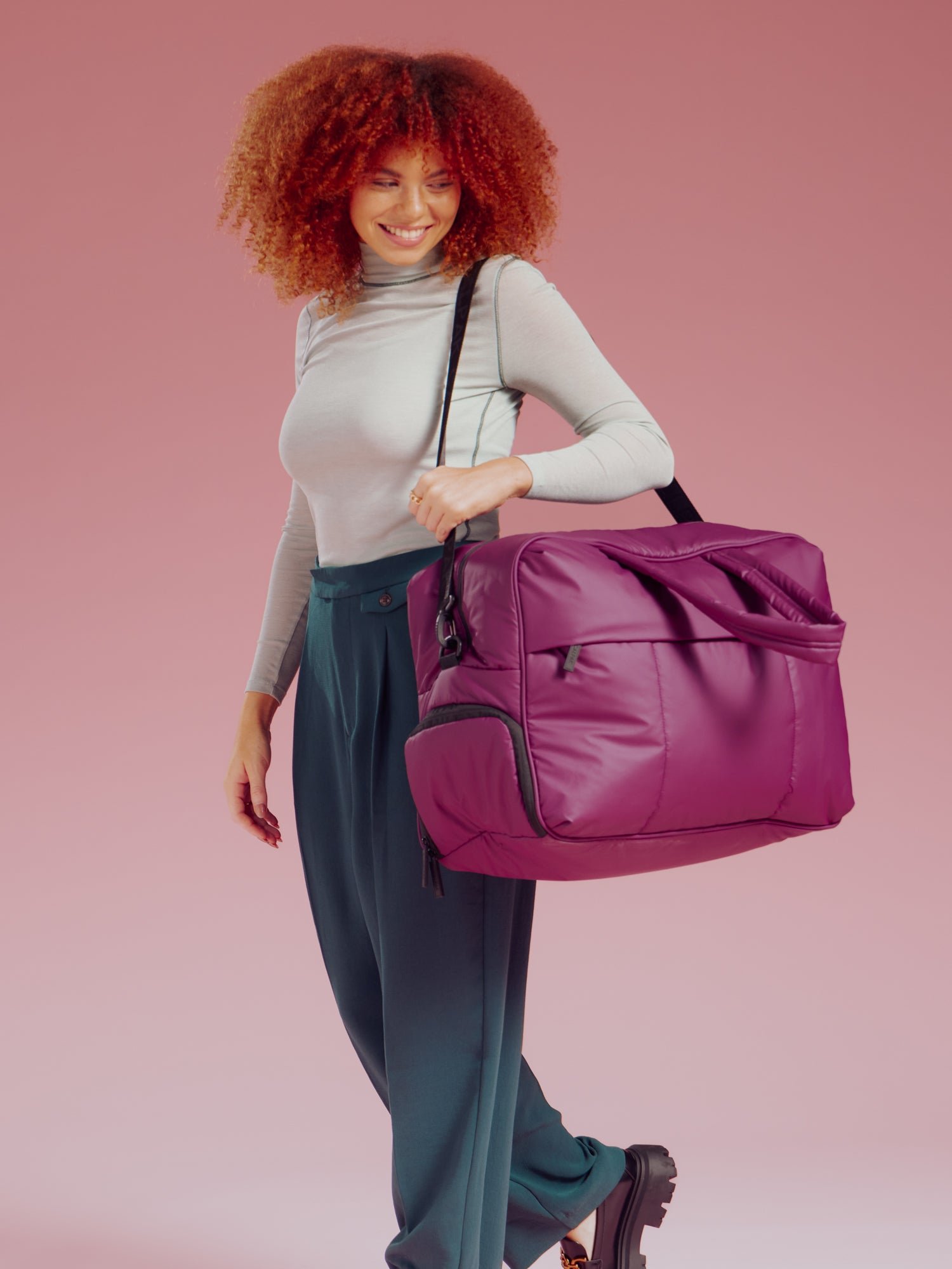 Model wearing CALPAK Large Luka Duffel bag over shoulder with detachable shoulder strap in purple plum