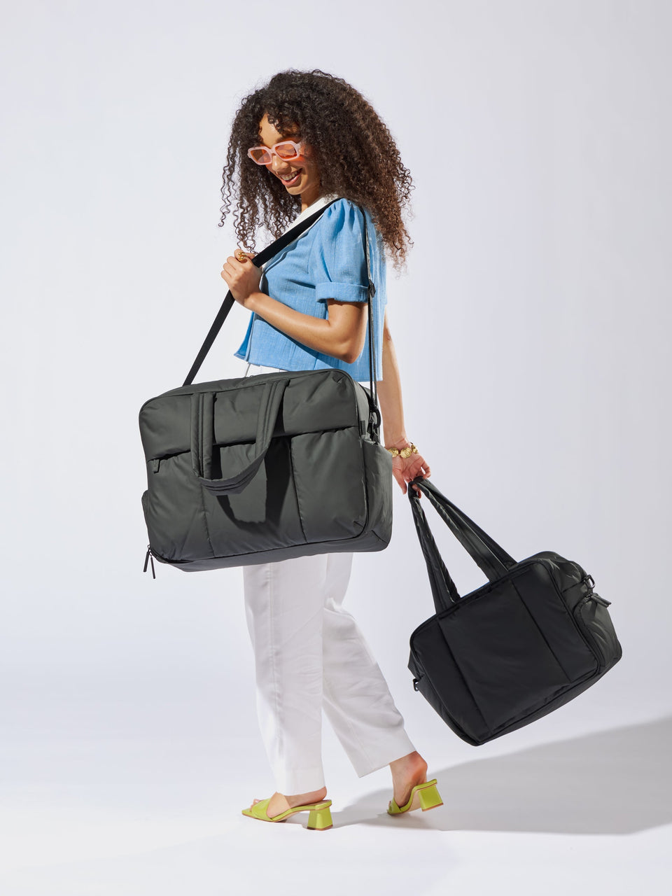 Model carrying CALPAK Luka large duffle bag and Luka duffel with detachable strap and zippered front pocket in black; DLL2201-MATTE-BLACK