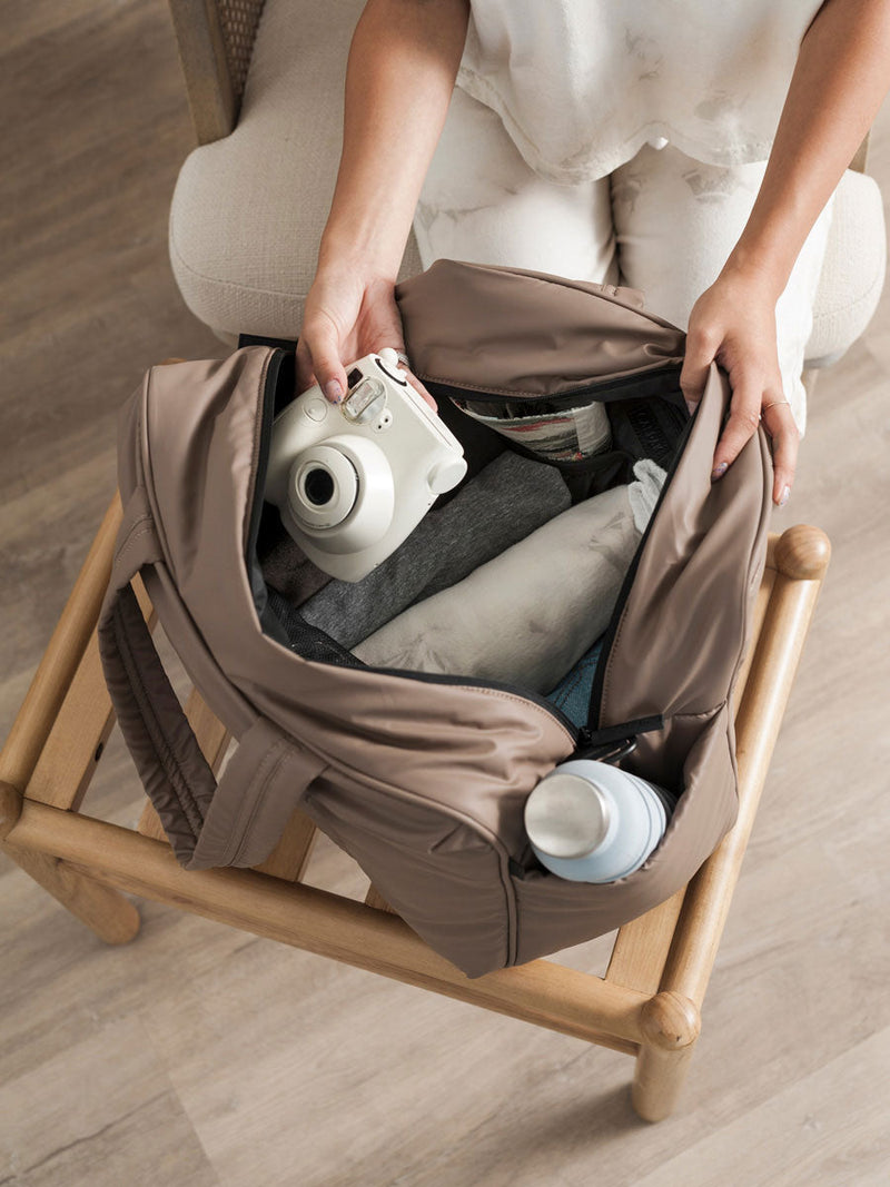Model placing camera into chocolate CALPAK Luka Duffel Bag