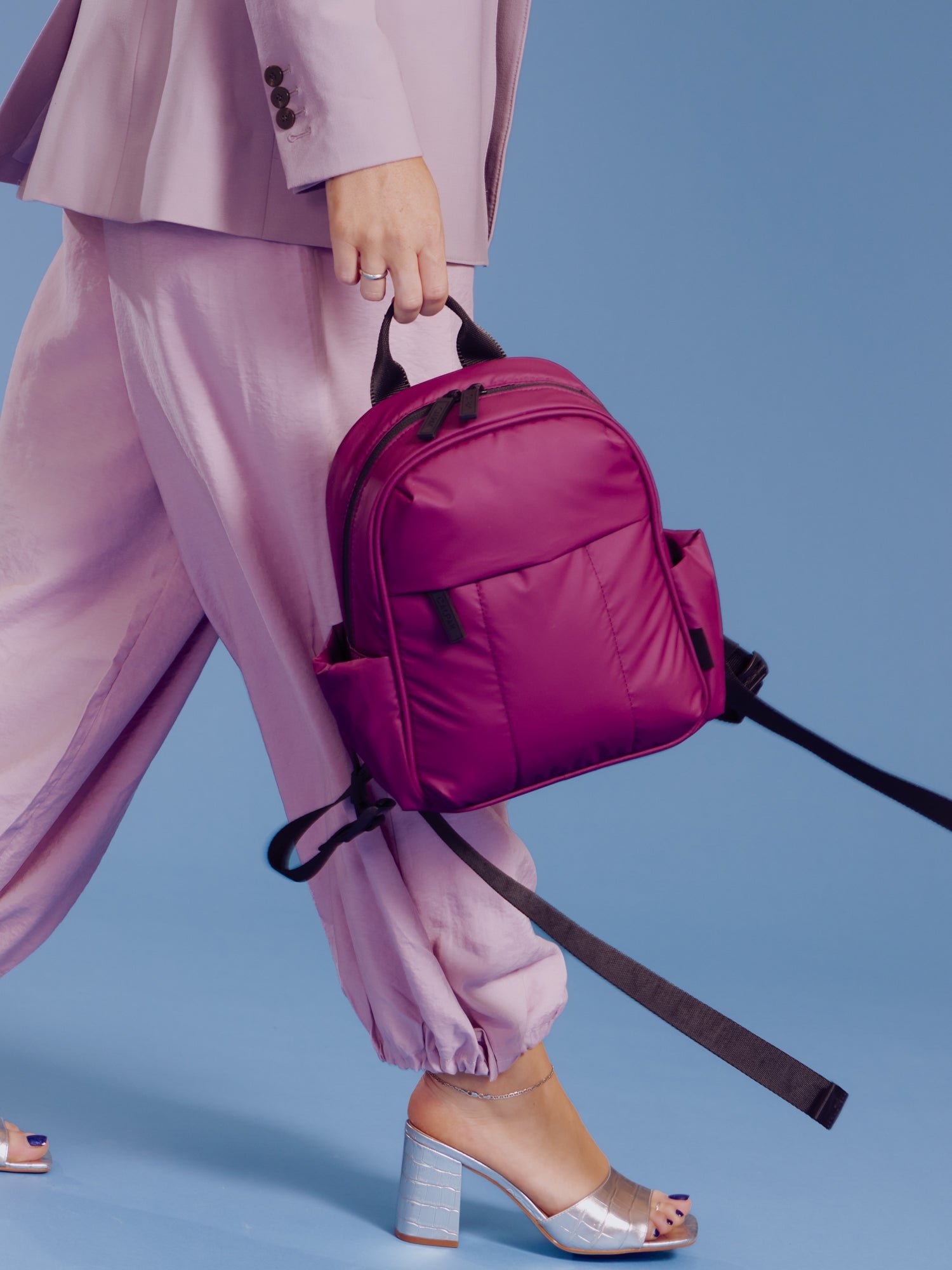 Model walking and holding CALPAK Luka Mini Backpack in purple plum in right hand