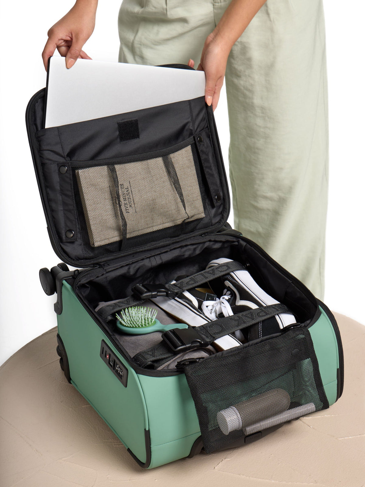 Model placing laptop and belongings inside the CALPAK Luka Mini Carry-On Luggage in green sage; LSM1014-SAGE