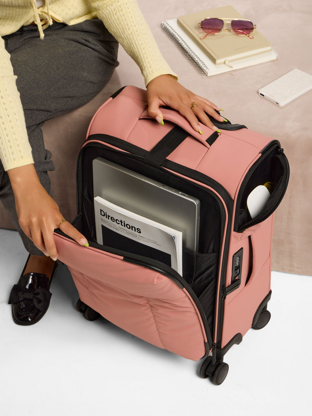 Model displaying laptop and book in front pocket of CALPAK Luka Soft-Sided Carry-On Luggage in peony; LSM1020-PEONY