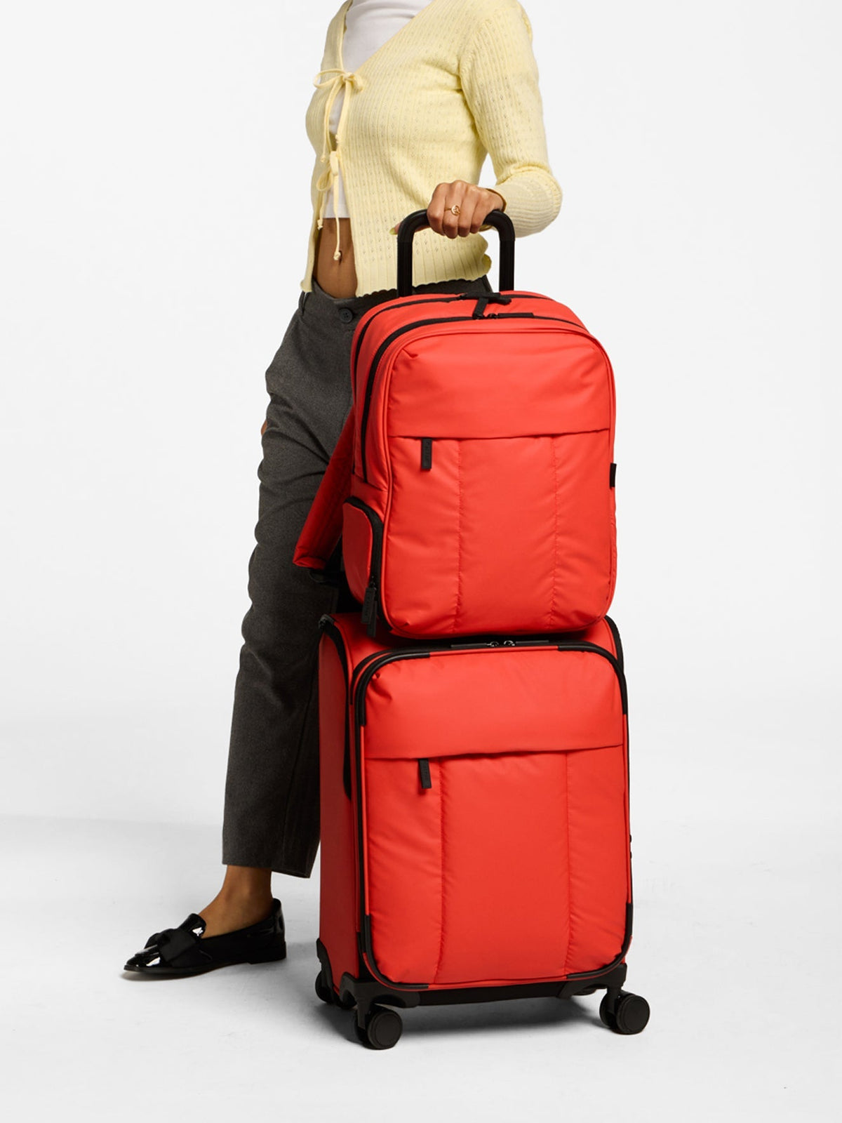 Model rolling CALPAK Luka soft luggage with front zippered pockets in red rouge; LSM1020-ROUGE