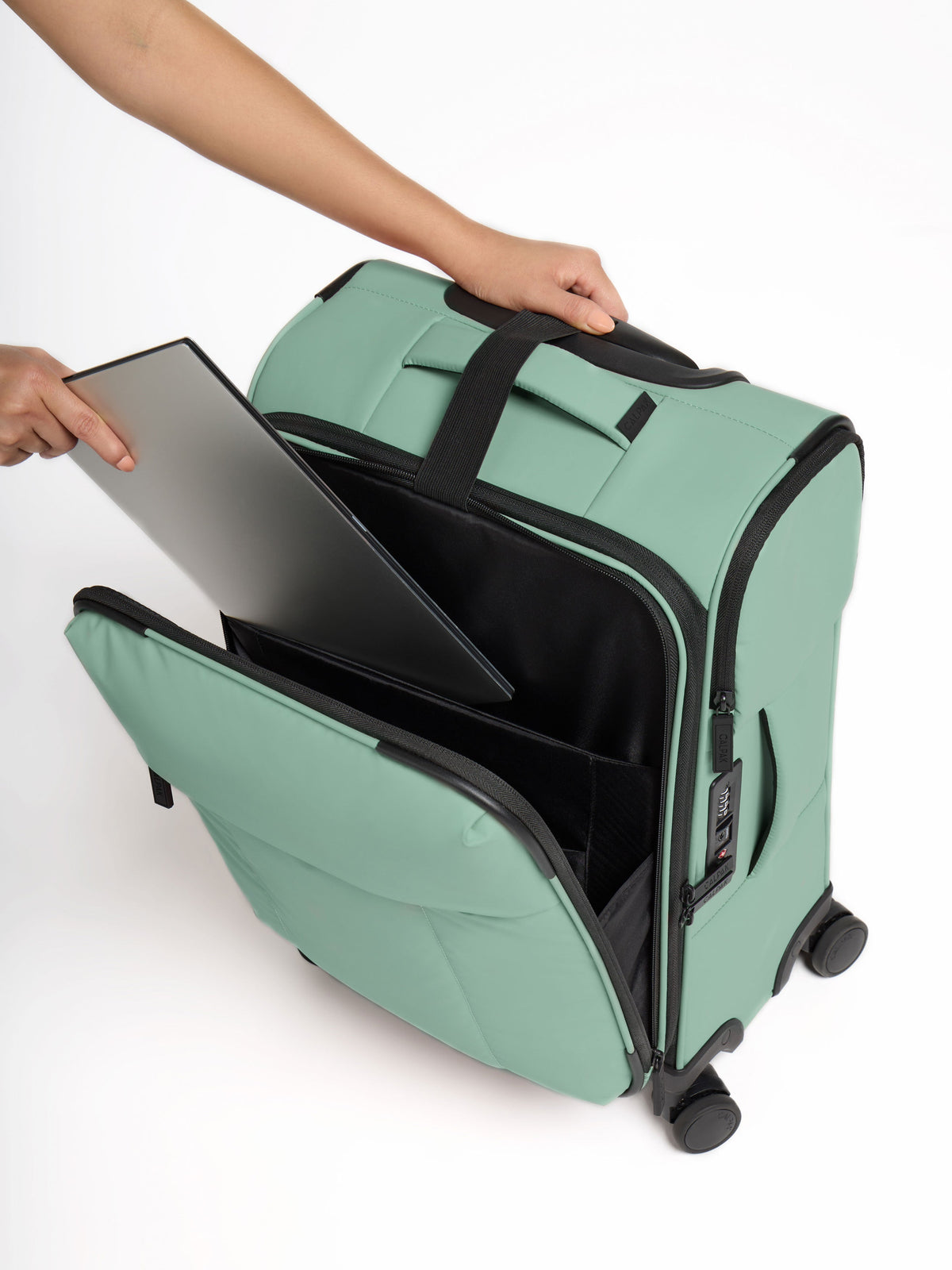 Model placing laptop in front pocket of CALPAK Luka Soft-Sided Carry-On Luggage in green; LSM1020-SAGE