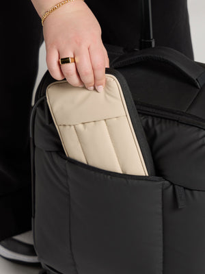 Model placing oatmeal CALPAK Luka Zippered Passport Wallet within front pocket of CALPAK Luka Soft-Sided Mini Carry-On Luggage in matte black; PZW2301-OATMEAL