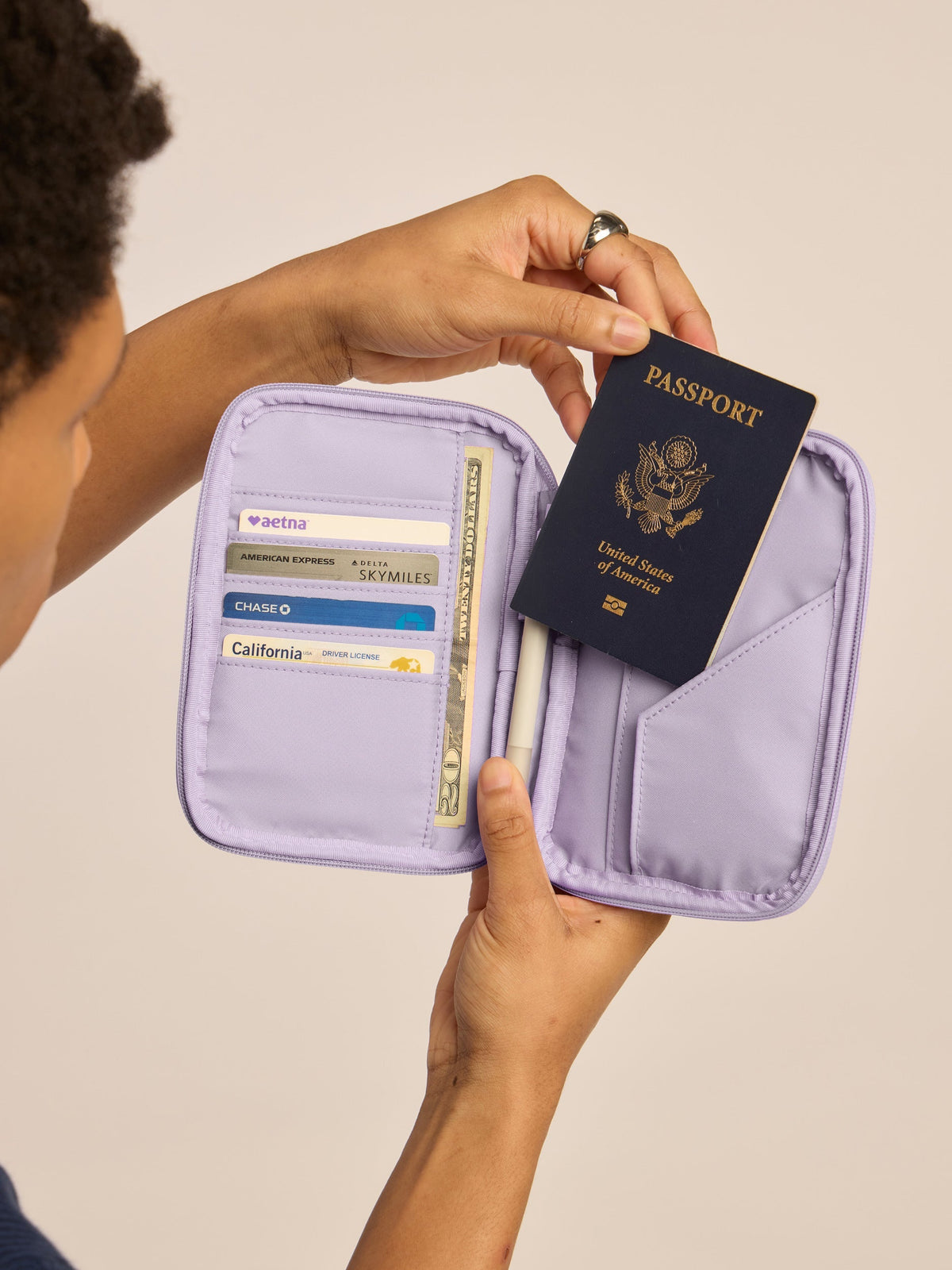 Model holding opened CALPAK Luka Passport Zippered Wallet with cards and passport in lavender purple Orchid; PZW2301-ORCHID