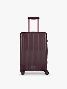 CALPAK Vault deep red Dark Cherry hard-shell spinner Carry On Luggage with a telescoping handle extended, featuring a deep red leatherette side handle and trim, set against a plain light gray background; LVT1020-DARK-CHERRY