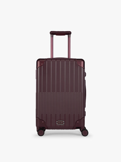 CALPAK Vault deep red Dark Cherry hard-shell spinner Carry On Luggage with a telescoping handle extended, featuring a deep red leatherette side handle and trim, set against a plain light gray background; LVT1020-DARK-CHERRY view 1