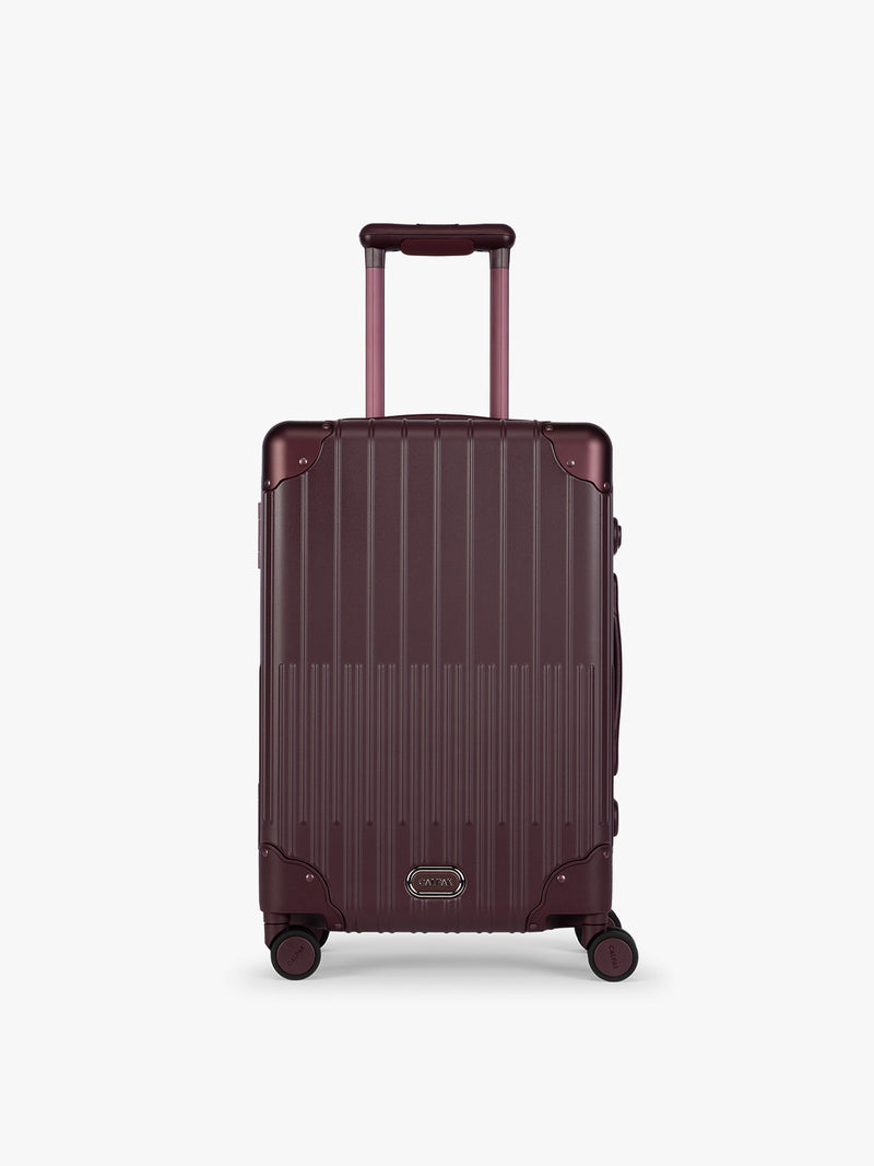 CALPAK Vault deep red Dark Cherry hard-shell spinner Carry On Luggage with a telescoping handle extended, featuring a deep red leatherette side handle and trim, set against a plain light gray background