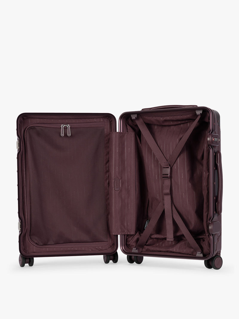 Opened CALPAK Vault deep red Dark Cherry hard-shell spinner Carry On Luggage with a telescoping handle extended, featuring a deep red leatherette side handle and trim, set against a plain light gray background