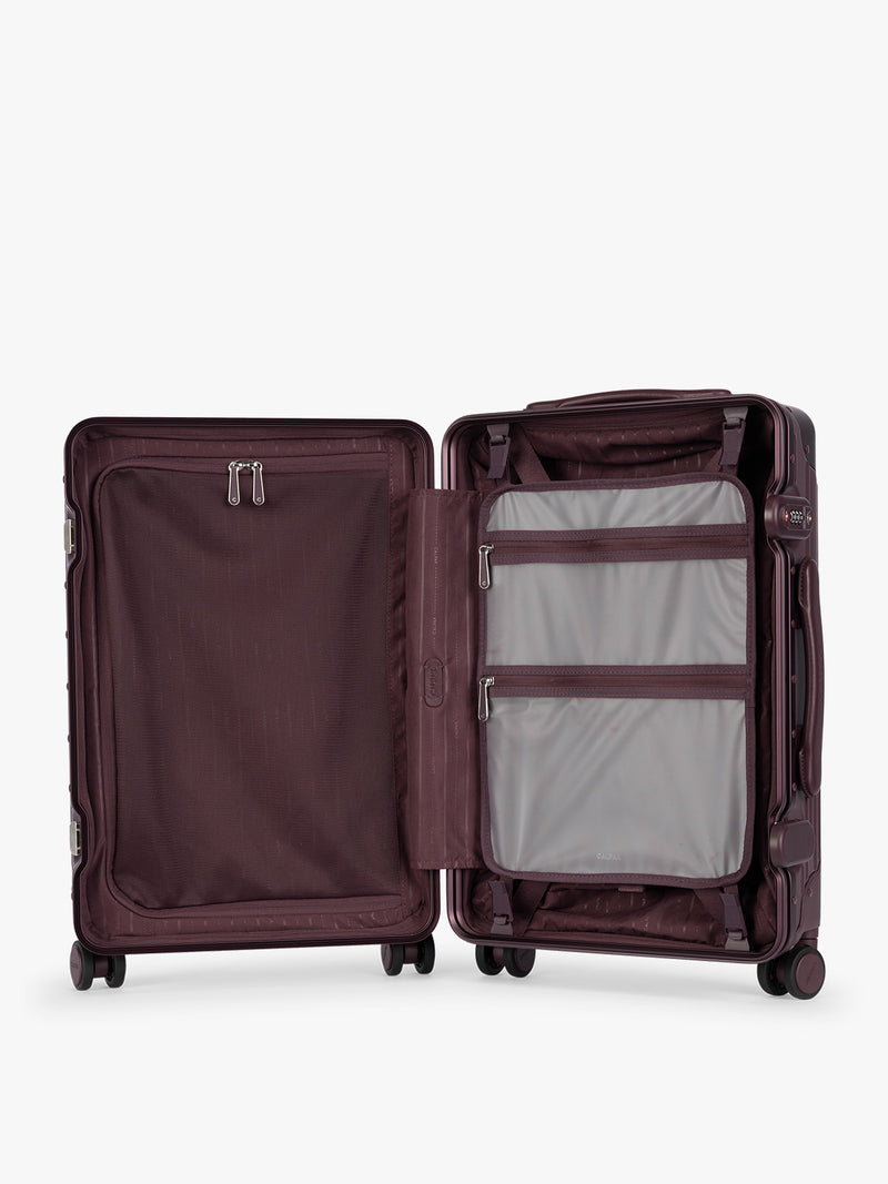 Opened showing grey attachment with zipper of CALPAK Vault deep red Dark Cherry hard-shell spinner Carry On Luggage with a telescoping handle extended, featuring a deep red leatherette side handle and trim, set against a plain light gray background