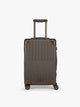 CALPAK Vault brown Mushroom hard-shell spinner Carry On Luggage with a telescoping handle extended, featuring a black leatherette side handle and trim, set against a plain light gray background; LVT1020-MUSHROOM